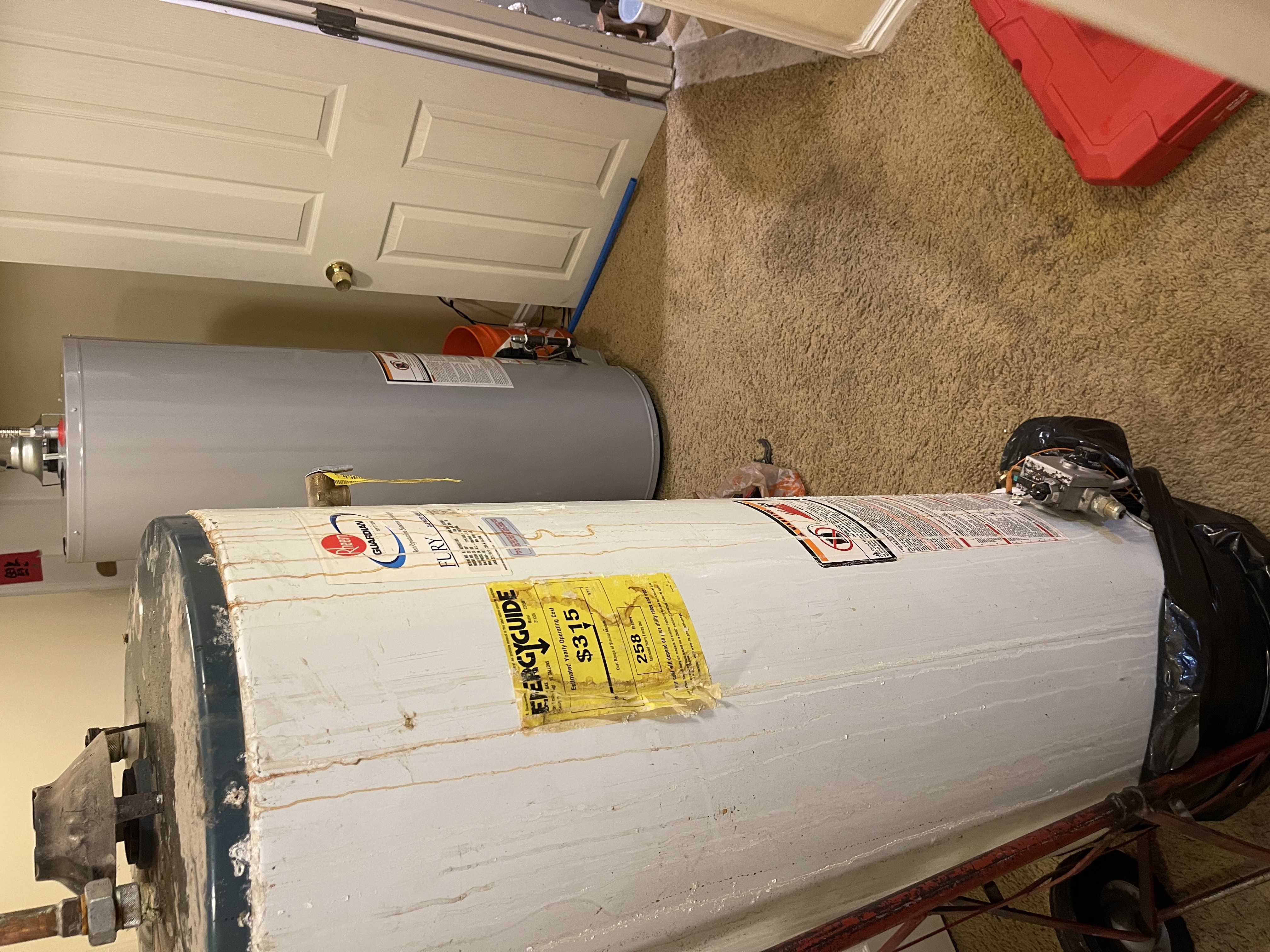 Old rusted water heater being removed next to a brand new replacement in a Lehi, Utah home