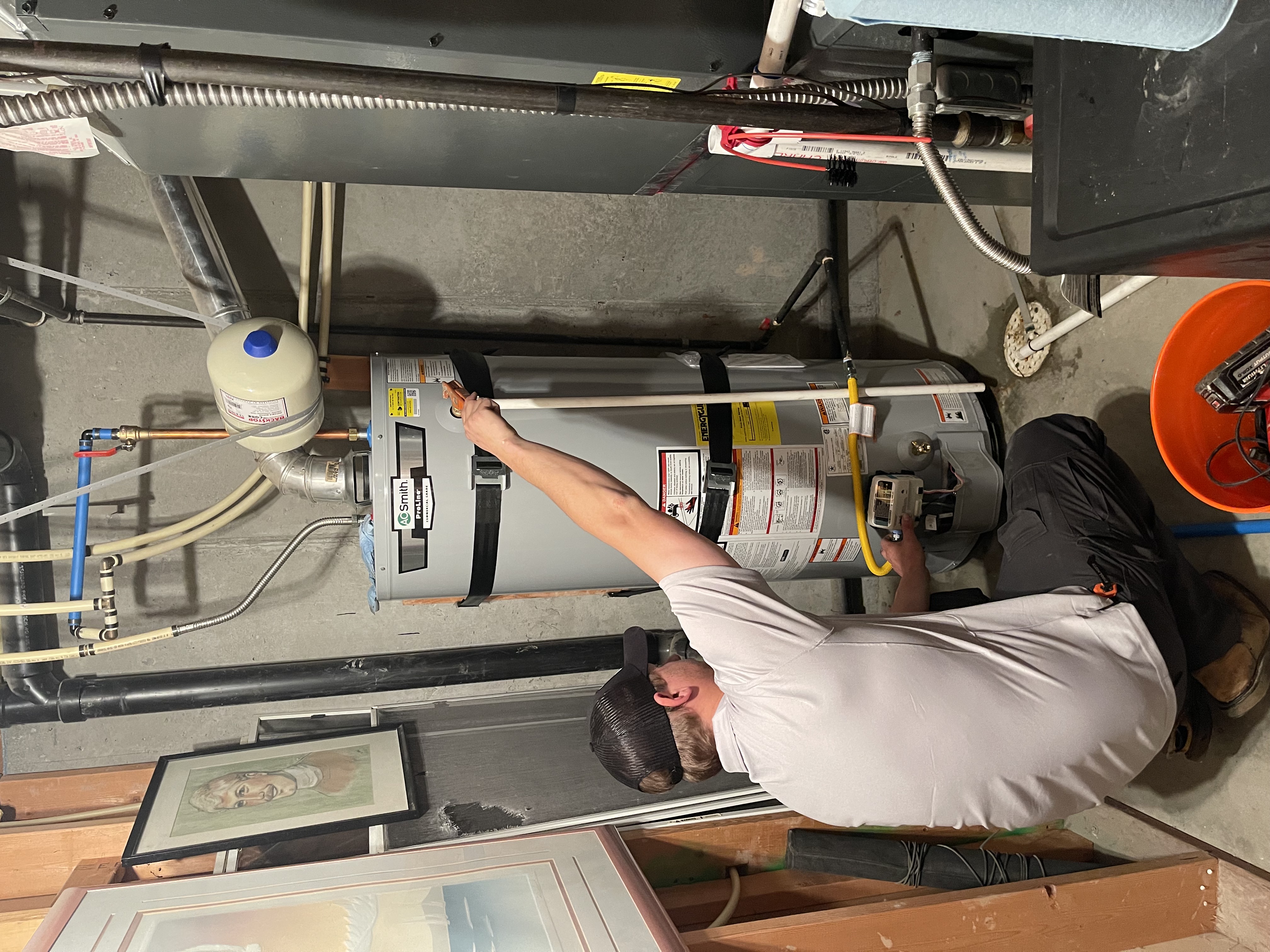 Utah Water Heaters Now technician kneeling to light the pilot on a newly installed A.O. Smith ProLine water heater