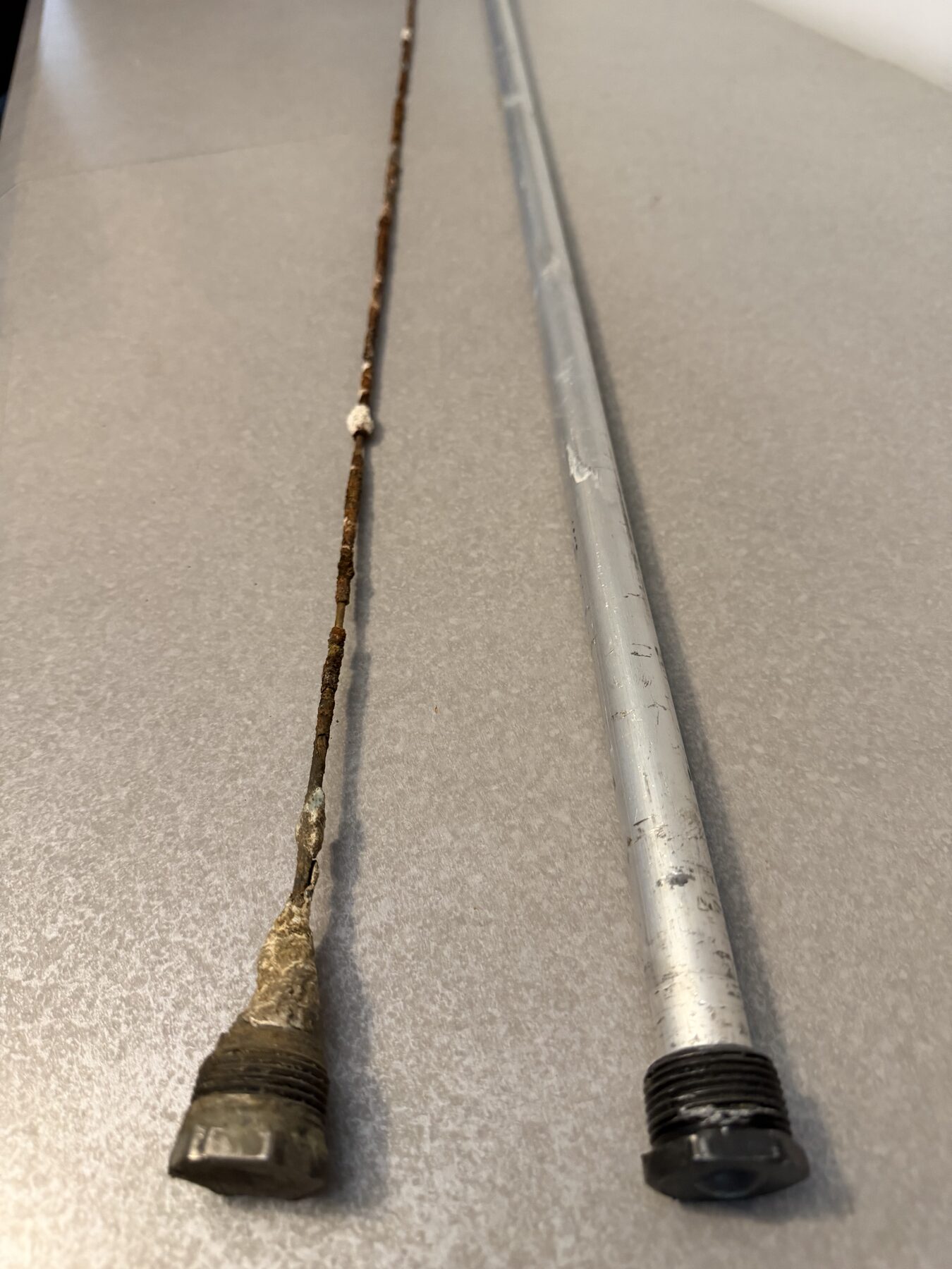 Two factory-installed sacrificial anode rods: a heavily corroded rod after years of use and a new rod before corrosion